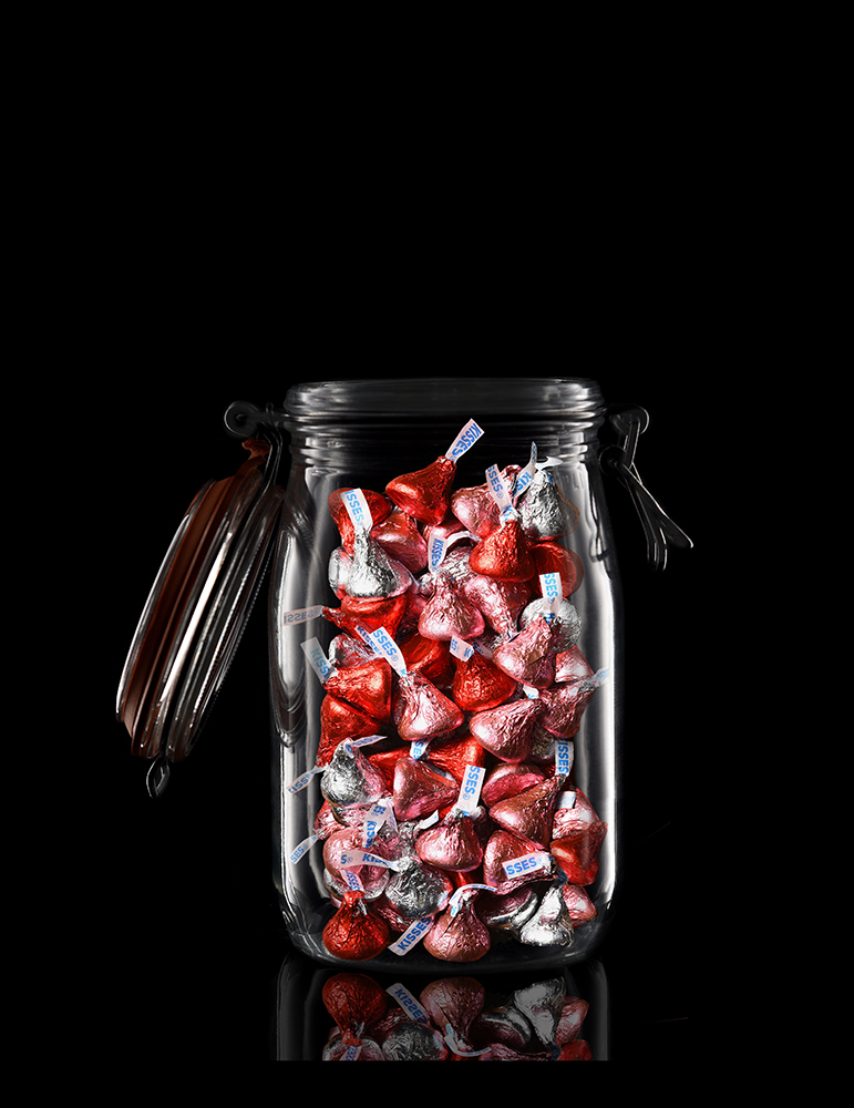 Valentines Concept. A  glass storage jar filled with Hershey Kisses on black with reflection.